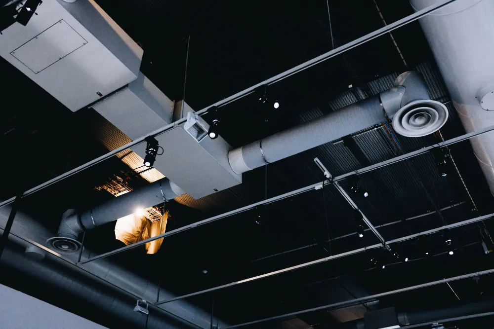 Intricate network of HVAC system components visible in a commercial building ceiling, reflecting Sensgreen's focus on smart energy systems with advanced thermostats, building management systems for efficient control, air quality, and energy savings in modern workspaces.